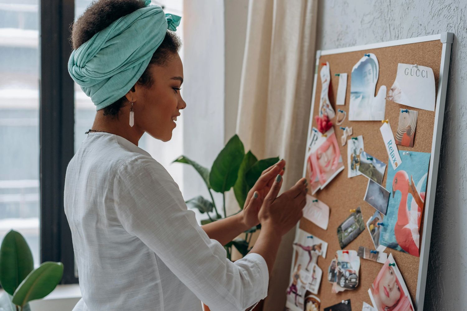 Woman in a headwrap arranging photos on a corkboard.
