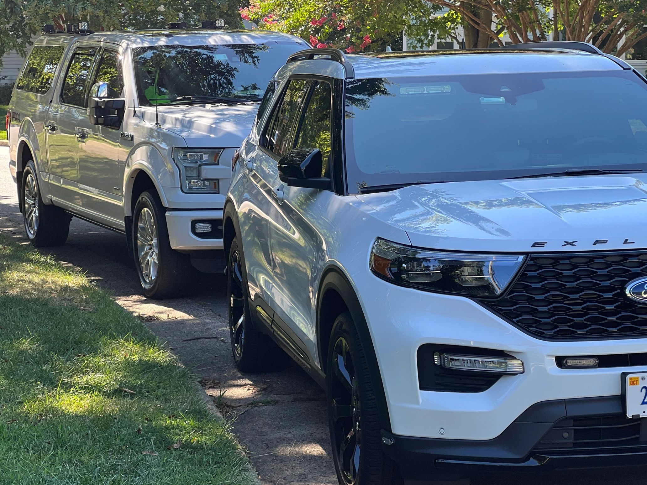 Two white Ford SUVs parked on a tree-lined street.