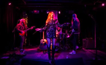 A band performs live on a dimly lit stage with purple lighting.