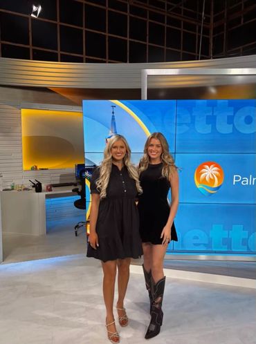 Two women posing in a TV studio with a bright backdrop.