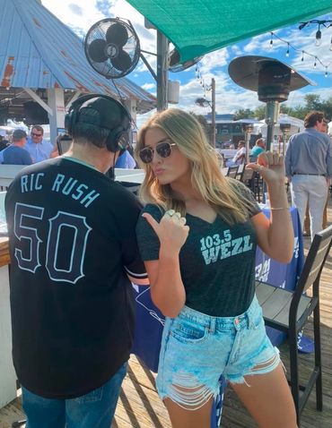 Two people wearing matching 103.5 WEZZL shirts at an outdoor event.