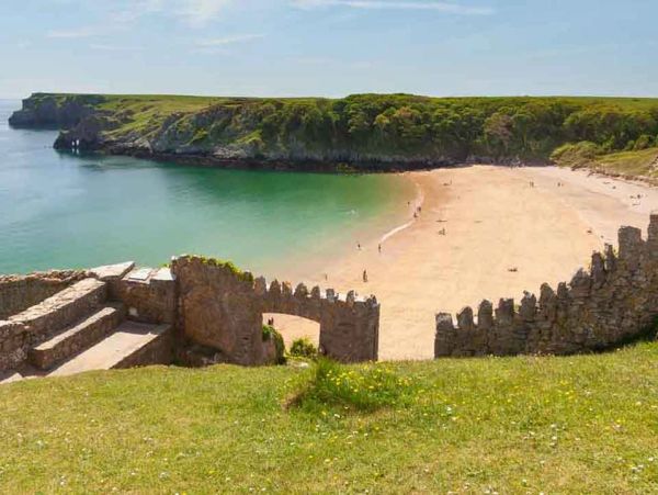 Scenic coastal beach with ancient stone walls and green cliffs.