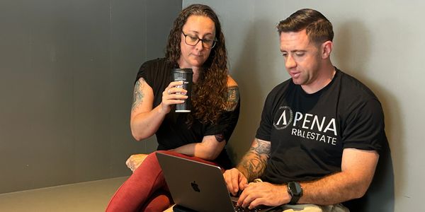 Two people collaborating with a laptop, one drinking coffee.
