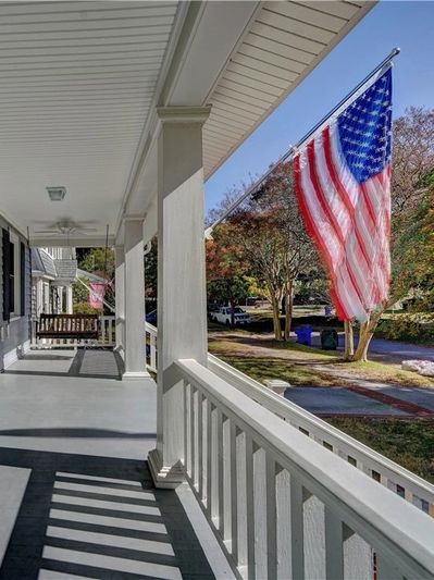 American flag waving on a sunny porch with white railings and columns.