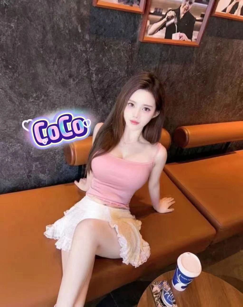 Woman in pink top and white skirt sitting on a brown bench.