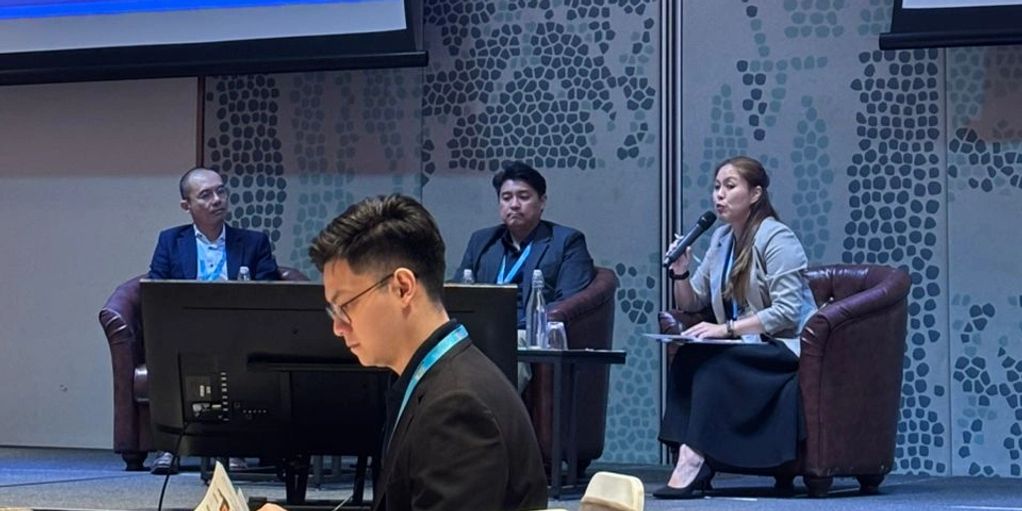 Panel discussion at a conference with audience member reading a document.