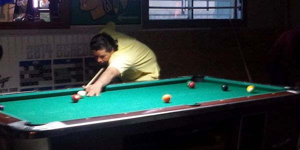 Man playing pool, aiming shot at billiard balls on green felt table.