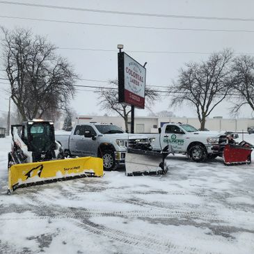 Three snow plows ready for clearing snow in a snowy parking lot.