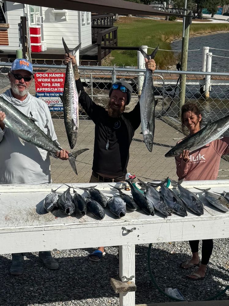Three people proudly display their large fresh catch of fish by the dock.