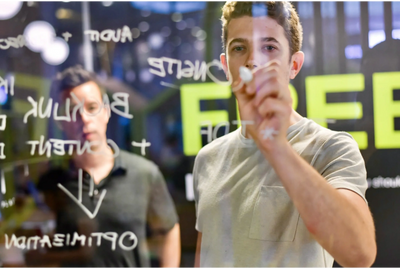 Image of two males writing on a transparent board. 