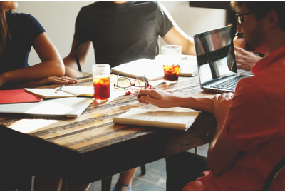 Image of a group of people around a table with laptops and pens and notebooks. 