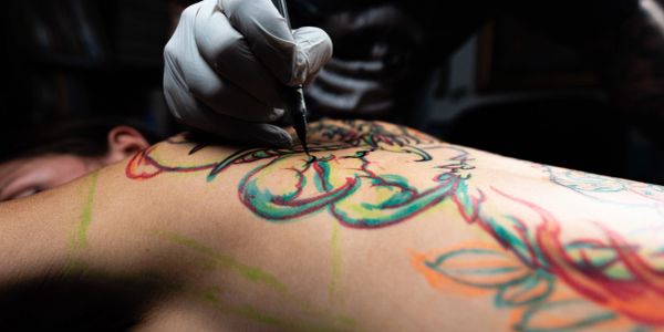 Artist tattooing colorful design on back.