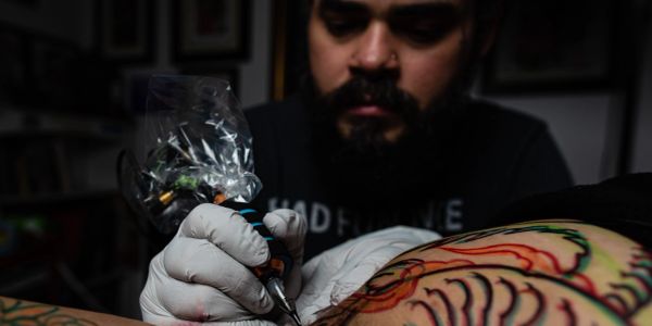 Tattoo artist working on colorful arm tattoo.