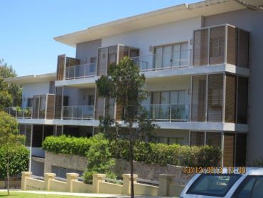 Modern multi-story apartment building with balconies and greenery.