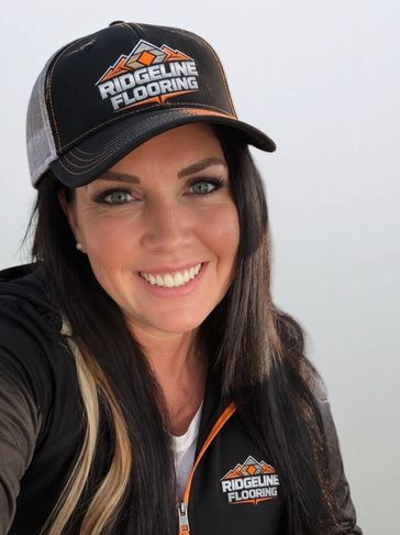 Woman smiling wearing Ridgeline Flooring cap and jacket.
