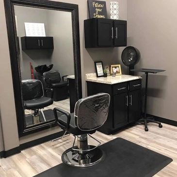 Modern hair salon station with black chair and large mirror.