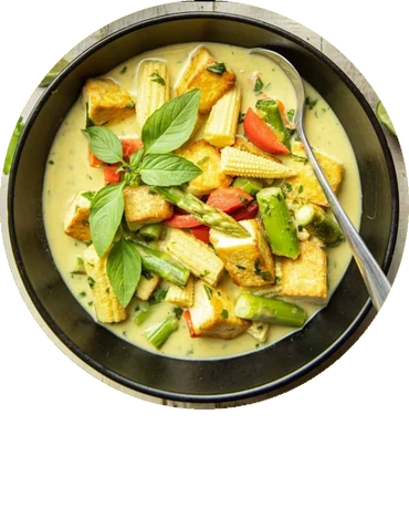 Creamy vegetable curry with tofu and fresh basil leaves in a black bowl.