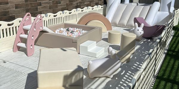 A soft play area with pastel-colored toys and a small slide inside a fenced space.