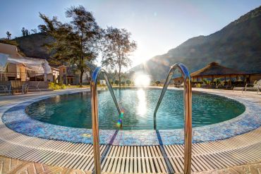 Sunlit round swimming pool with mountain backdrop.