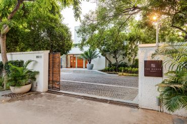 Entrance to a luxurious residence with lush greenery and a cobblestone driveway.
