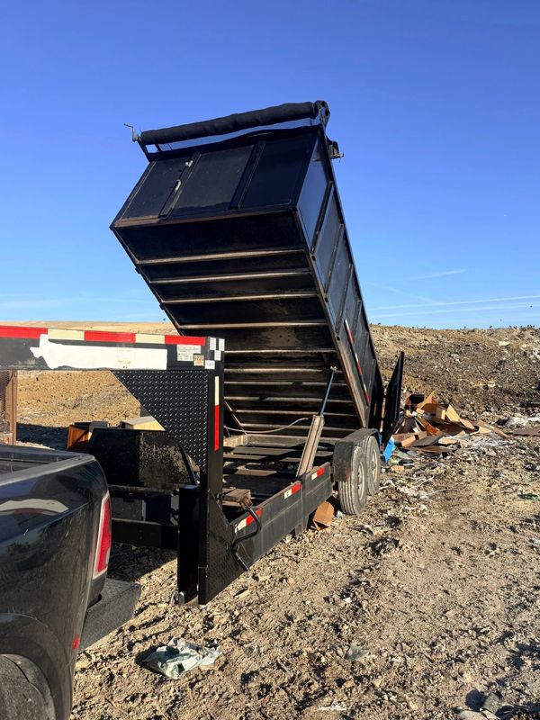 Black dump trailer unloading debris on dirt ground.