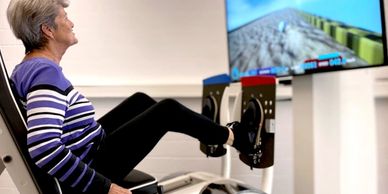 Elderly woman exercising with a leg press machine and virtual screen.