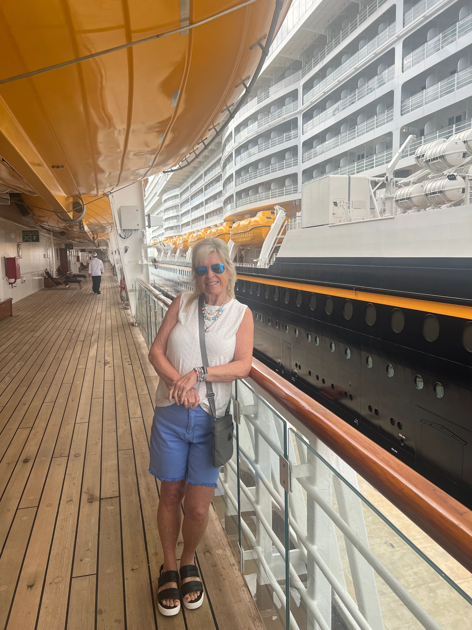 Woman smiling on a cruise ship deck with lifeboats overhead.
