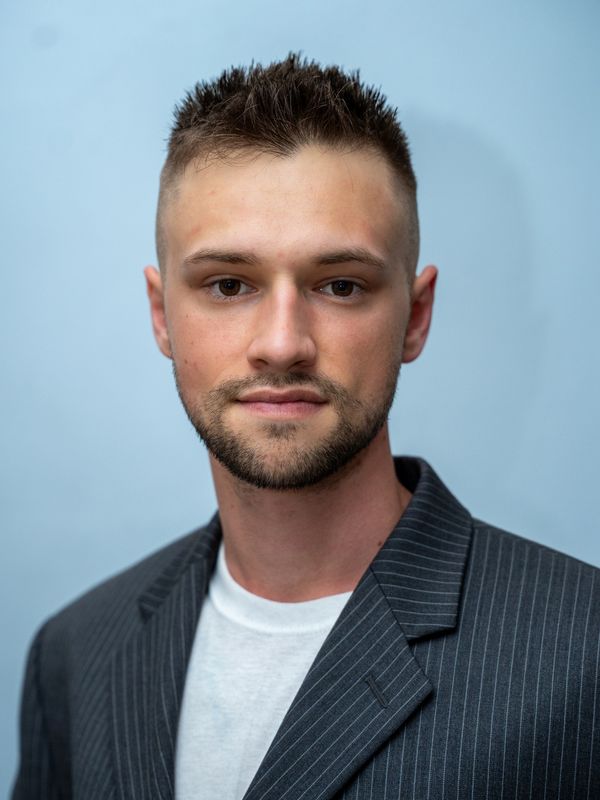 Young man with short hair and a beard wearing a pinstripe blazer.