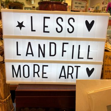 Lightbox sign says 'Less landfill, more art' surrounded by vintage items.