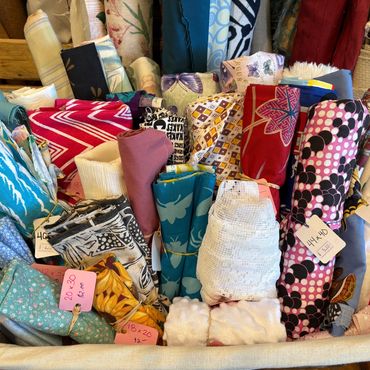 Basket of colorful fabric rolls with price tags at a market or store.