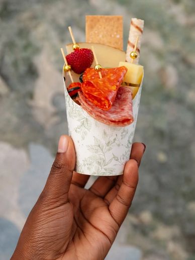 Hand holding a decorative cup with assorted snacks including strawberry, cheese, and crackers.