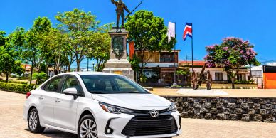 White Toyota sedan parked near a statue with flags.