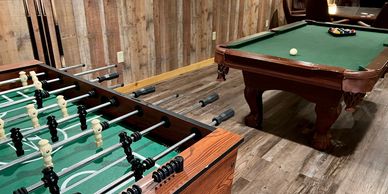 Game room with large playing table, sofa recliners, TV, billiards, and foosball.