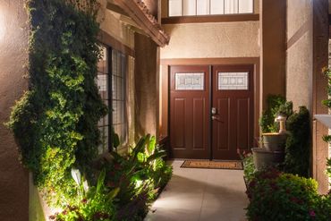 Cozy evening entrance with warm lighting and lush greenery.