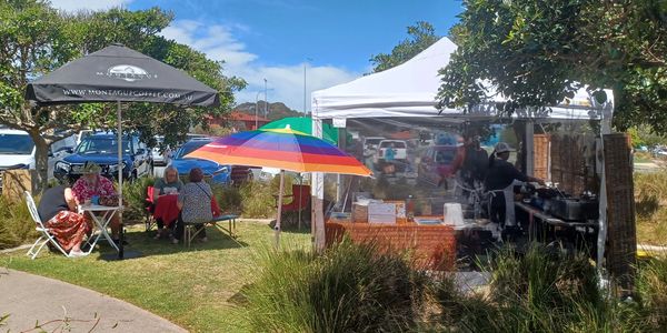 Outdoor market scene with people sitting under umbrellas and a food stall.