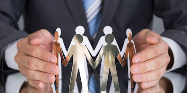 Hands protect paper cutout figures representing unity and diversity.