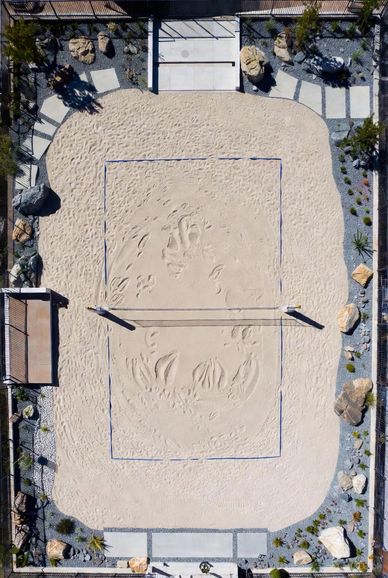 Aerial view of a sand volleyball court with surrounding rocks and plants.