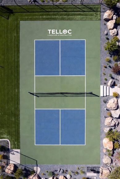 Aerial view of a blue and green tennis court with surrounding landscaping and rocks.