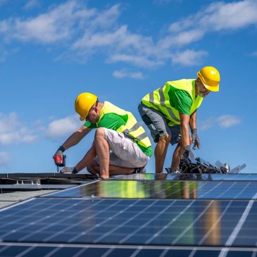 Workers installing solar panels on a roof under a clear sky.