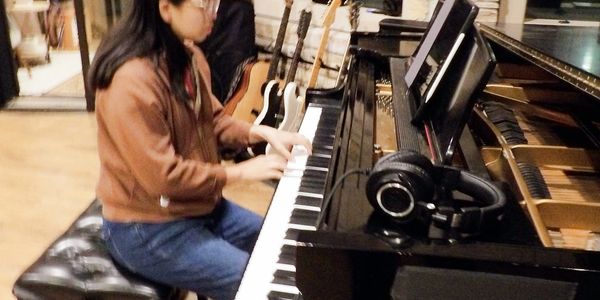 Person playing piano in a music room with guitars in the background.