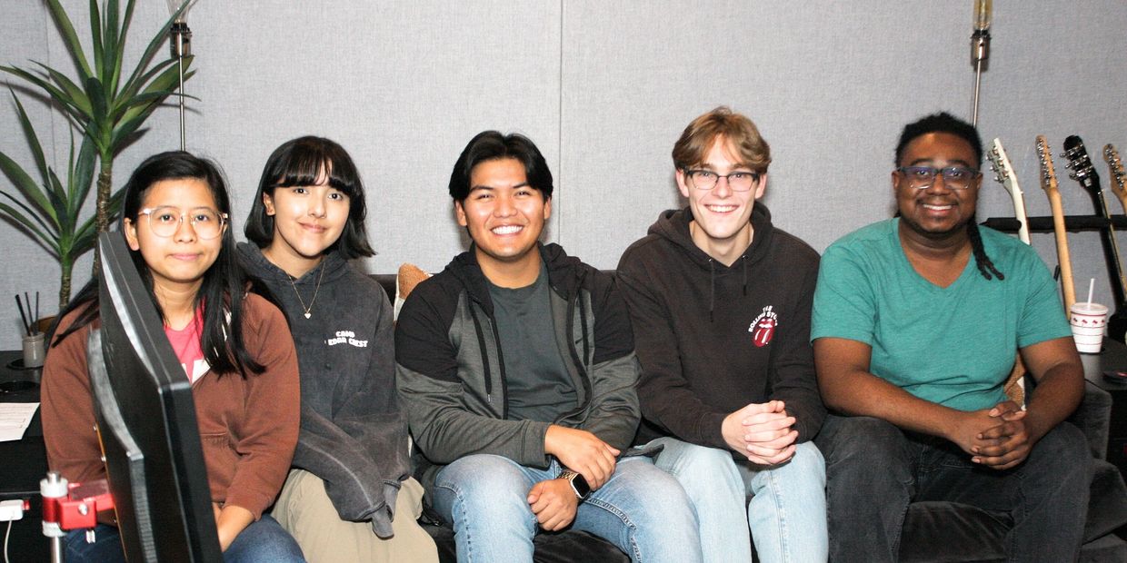Five young adults sitting side by side on a couch, smiling at the camera.