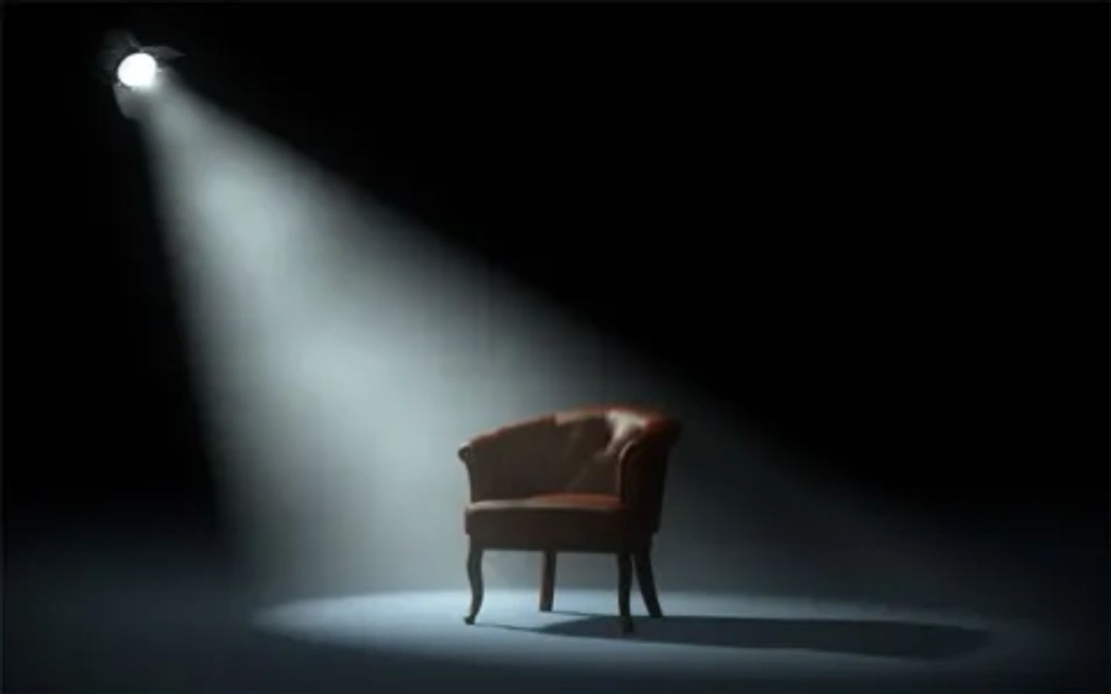 Single brown leather couch under a white spotlight on a black background