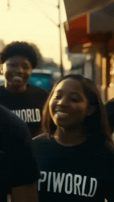 Two people smiling wearing PIWORLD shirts outdoors.