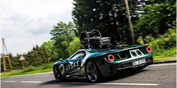 A sleek green sports car speeding on a curved road with a large camera mounted on top.