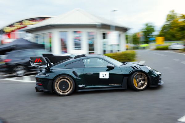 A sleek black sports car with racing decals drives on a street.