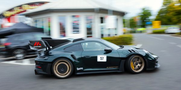 A sleek black sports car with racing decals drives on a street.
