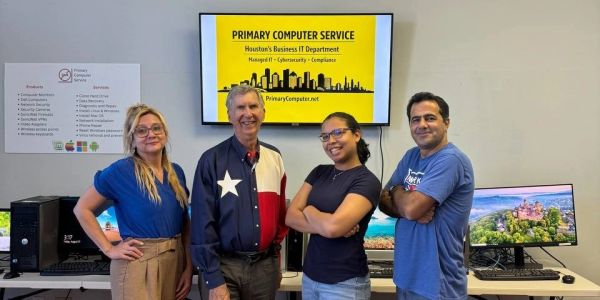 Four people posing in front of computers with a Primary Computer Service sign.