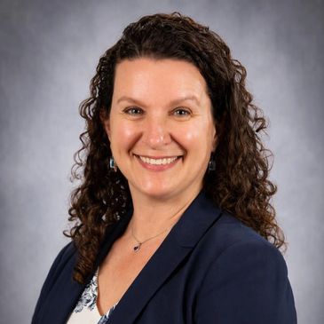 Professional woman smiling with curly hair and blazer.