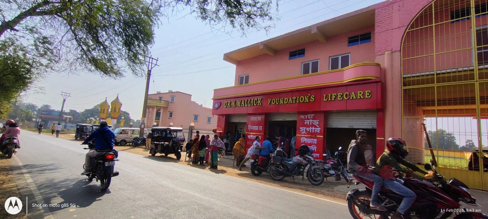 People and vehicles outside Dr. N. Mallick Foundation's Lifecare building on a sunny day.