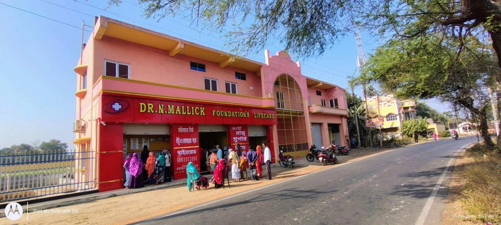 People lined up outside Dr. N. Mallick Foundation's Lifecare building on a sunny day.
